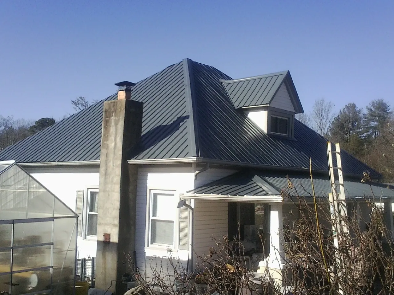 Dark blue standing seam metal roof on a white farmhouse with dormer — Slate & Tile Roof Repair by Roofing Brothers in Confluence