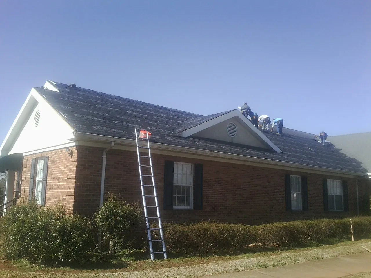 Crew tearing shingles off a brick ranch roof with a ladder set — Emergency Roof Repair work by our crew in Confluence