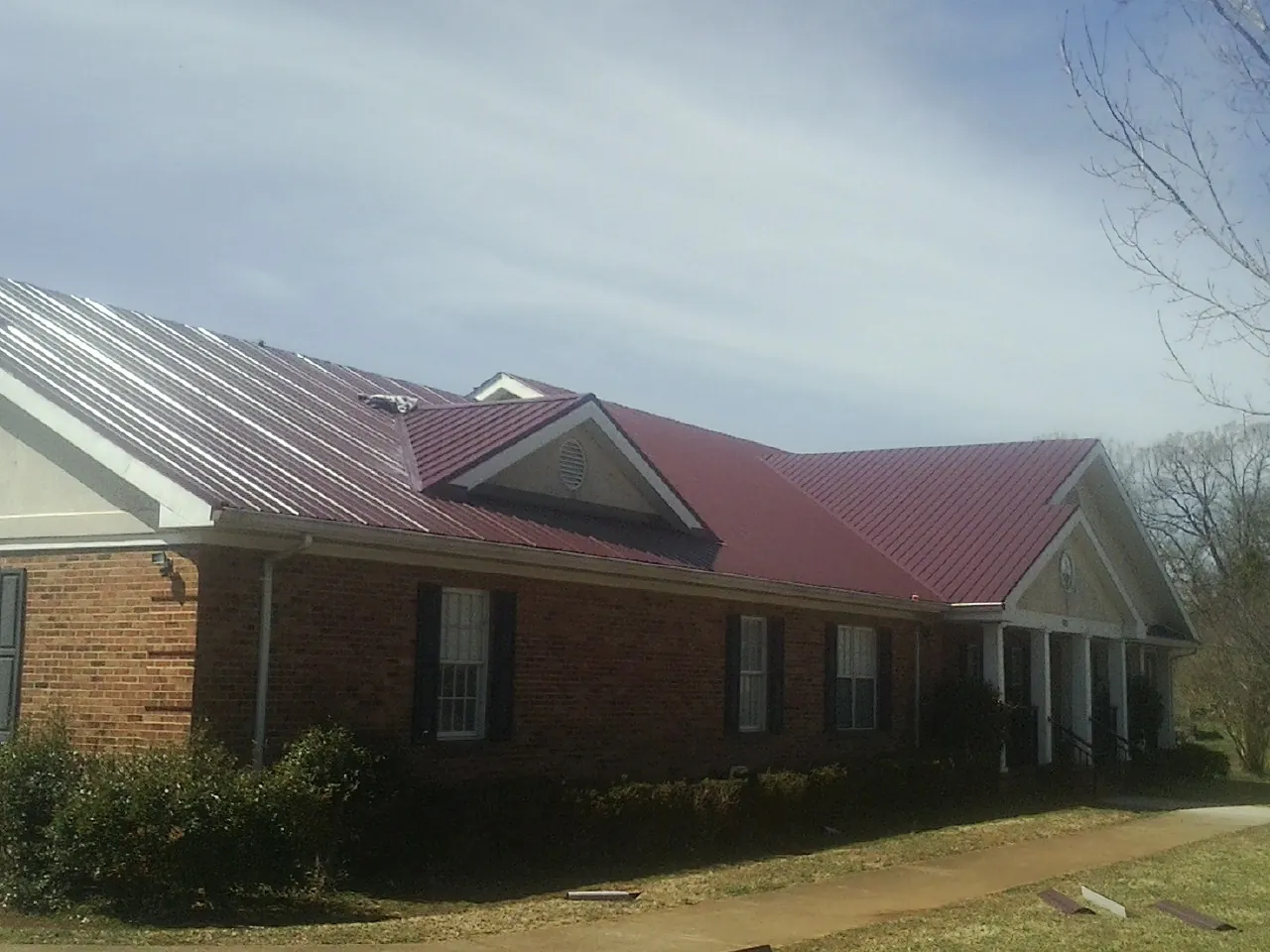 Red metal roof with gabled entries on a long brick building, from a Hail Damage Roof Repair job in Confluence
