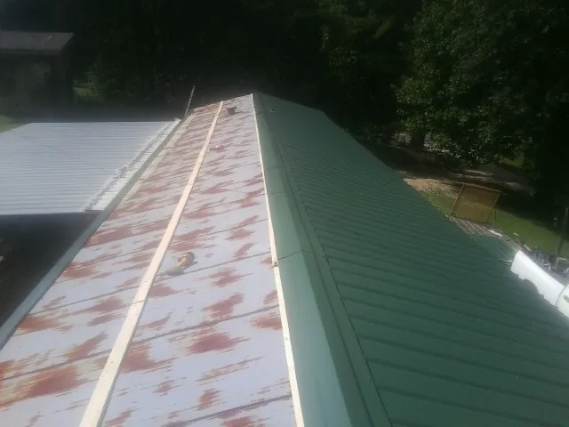 Old rusted panels beside newly installed green metal roofing — Wind Damage Roof Repair by Roofing Brothers in Confluence