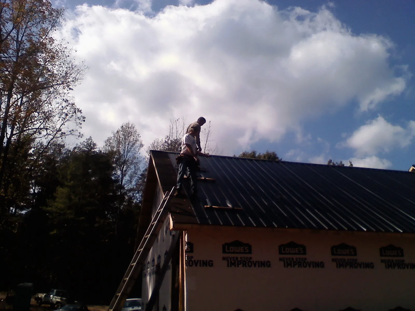 Roofer fastening dark metal panels high against a cloudy sky, from a Roof Inspection job in Confluence